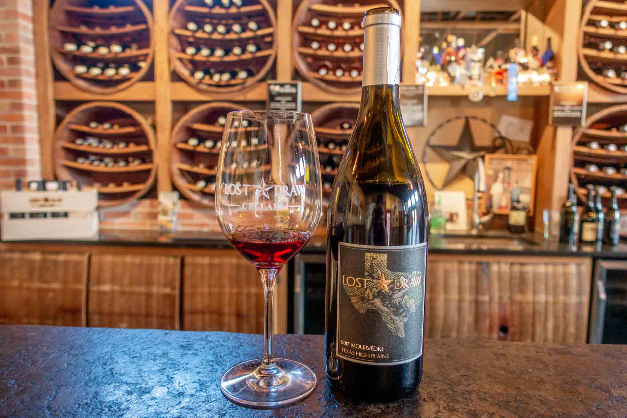 Bottle of Mourvedre wine and wine glass from Lost Draw Cellars on the bar. Lost Draw is one of the best Texas wineries to visit near Austin.