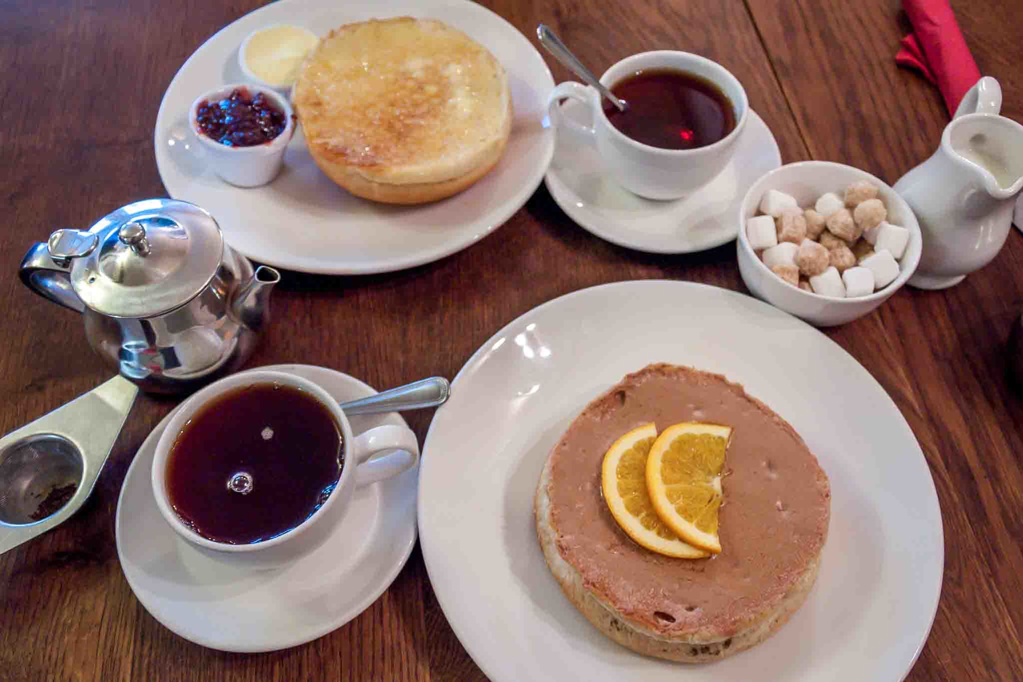 Two Sally Lunn buns topped with cinnamon spread and butter with two cups of tea on a table
