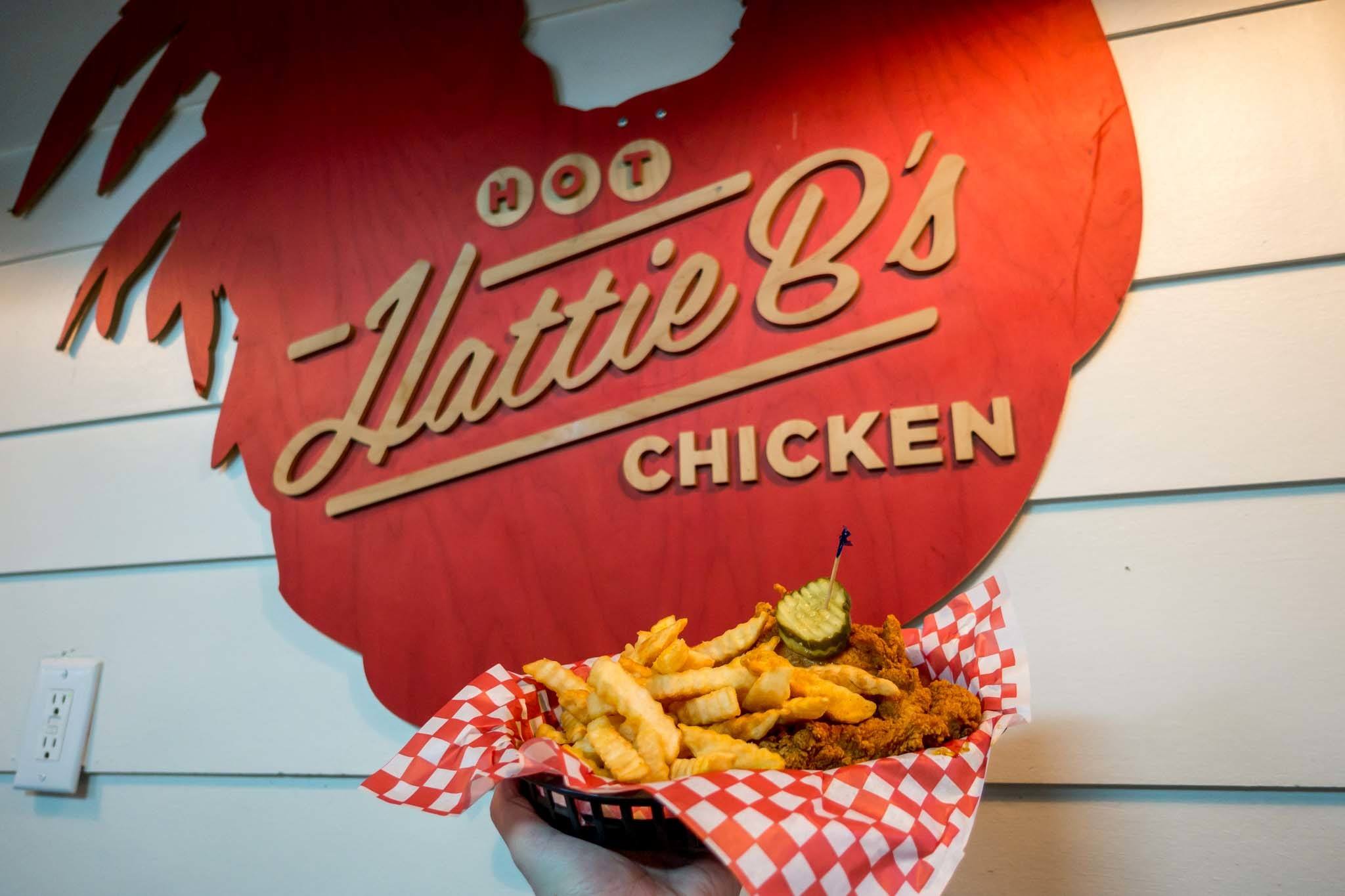 Basket of hot chicken in front of a Hattie B's sign. Trying it is one of the most delicious Nashville things to do.