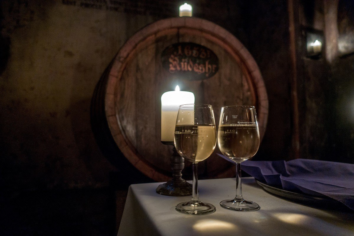 Two wine glasses in front of a wine barrel in a dark room illuminated by a candle. Visiting the wine cellar underneath Town Hall in Bremen Old Town is one of the most fun things to do in Bremen, Germany