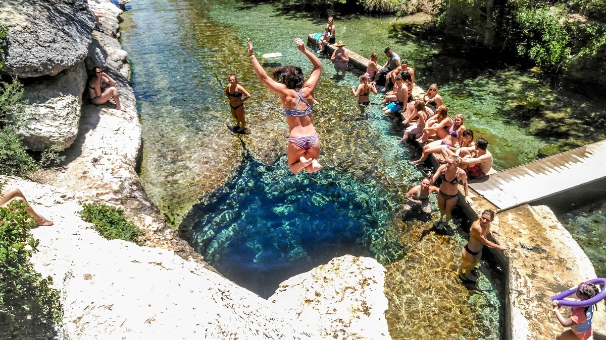 Woman jumping into water at Jacobs Well with onlookers