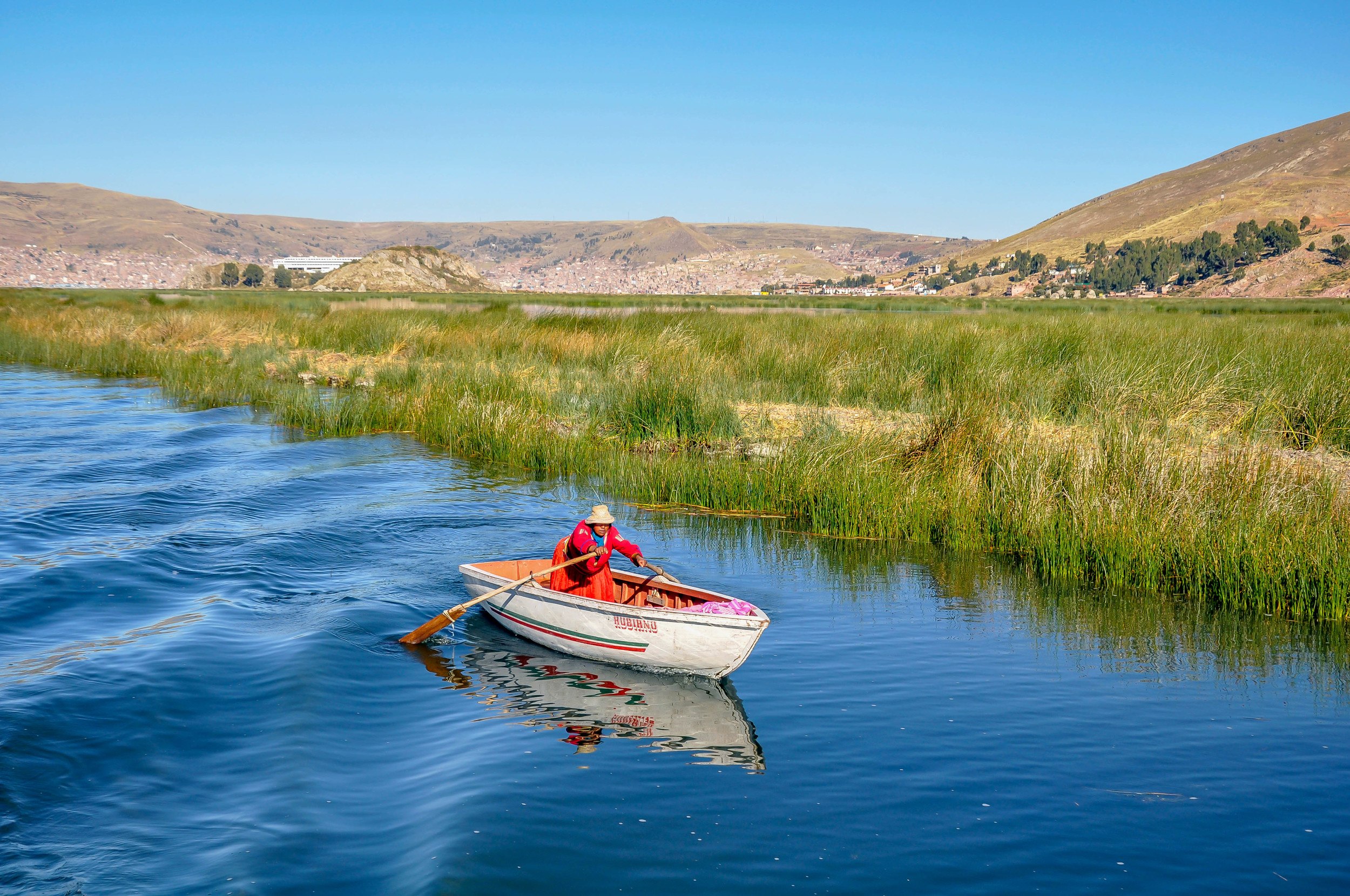 Woman in red dress rowing boat in Lake Titicaca, Peru