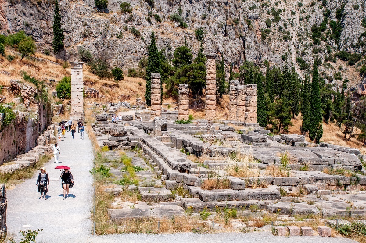 The Delphi Temple of Apollo. Note the people with umbrellas and the lack of shade. It is hot at the ancient Delphi ruins.