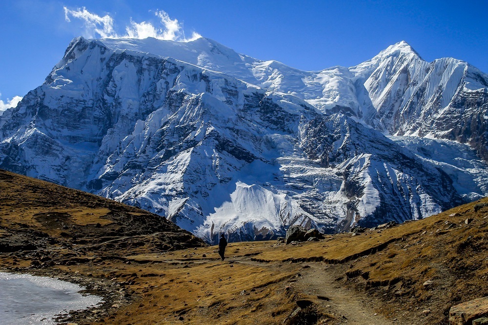 A sherpa walking along a trail leading to a snowy mountain summit