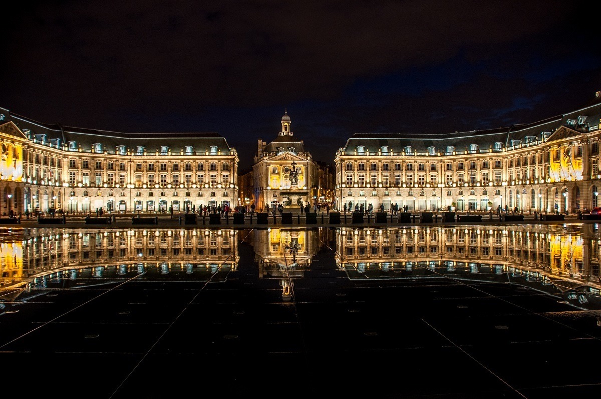 Large building reflected in the water on pavement at the Mirior d'Eau