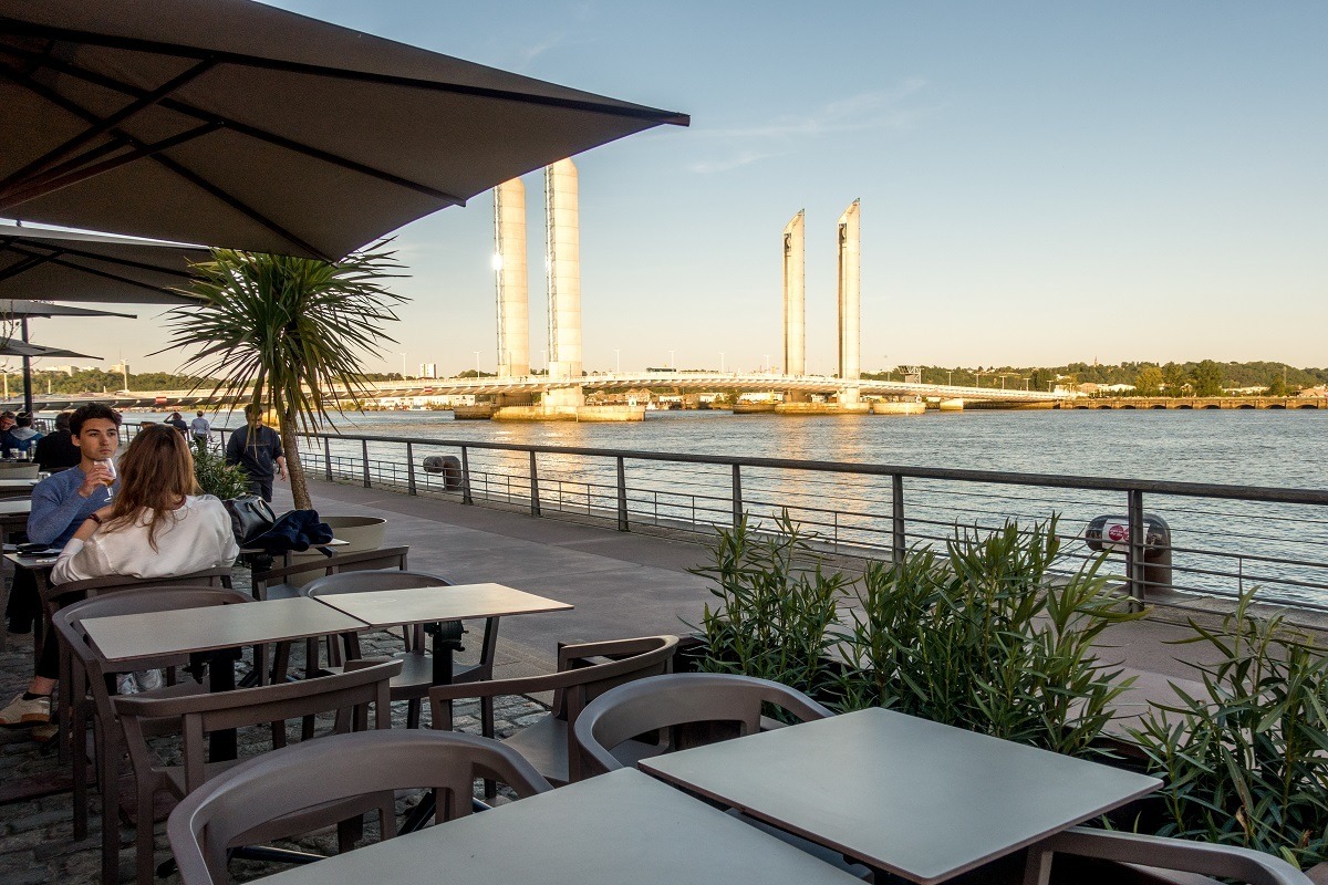 People sitting at an outdoor cafe by the bridge and river in Bordeaux