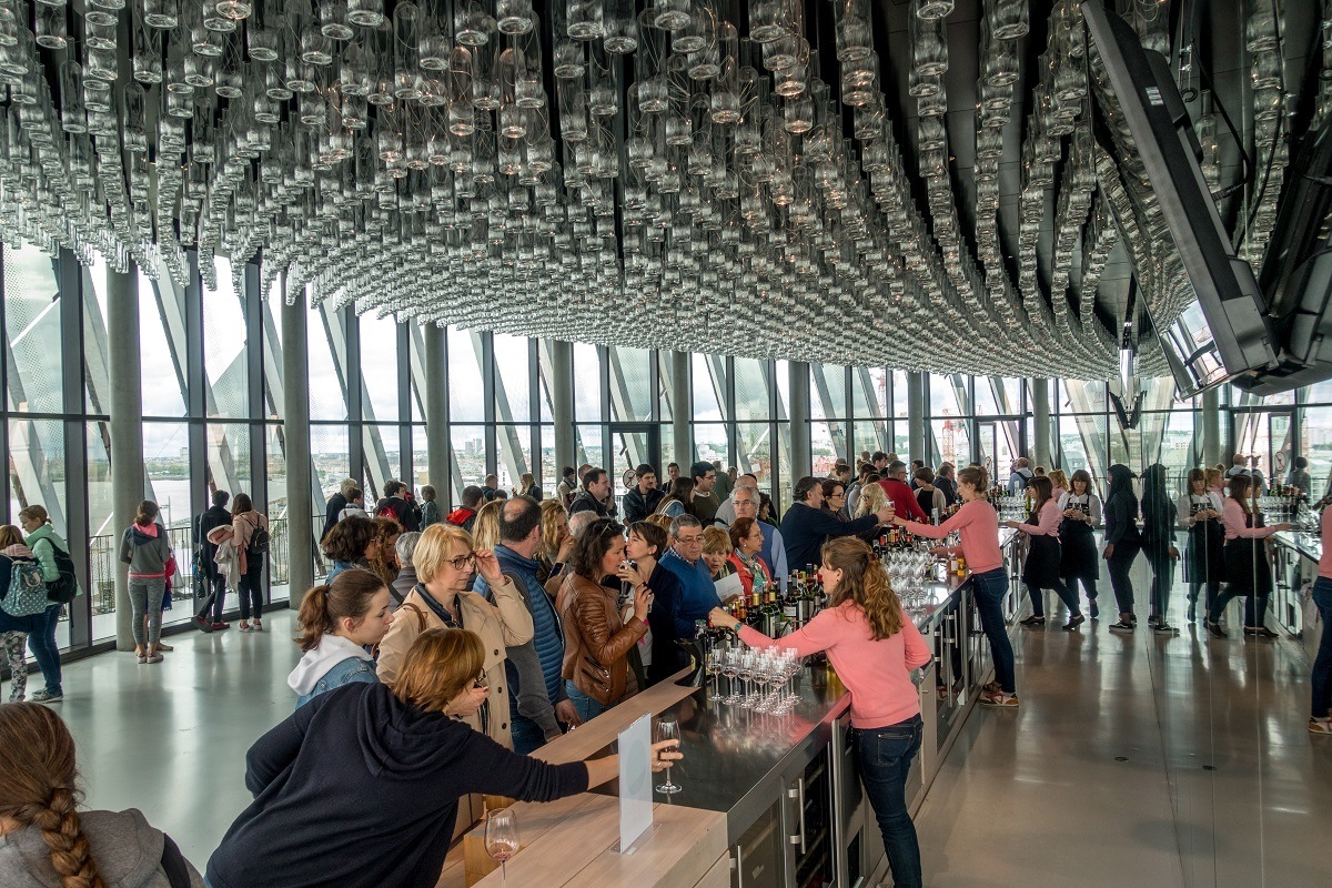 Visitors at wine bar of La Cite du Vin where glass bottles hang from the ceiling