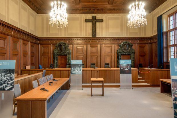 Courtroom 600 where the Nuremberg Trials were held features a judge's bench, place for the defendants, and posters explaining how the room appeared during the famous trials