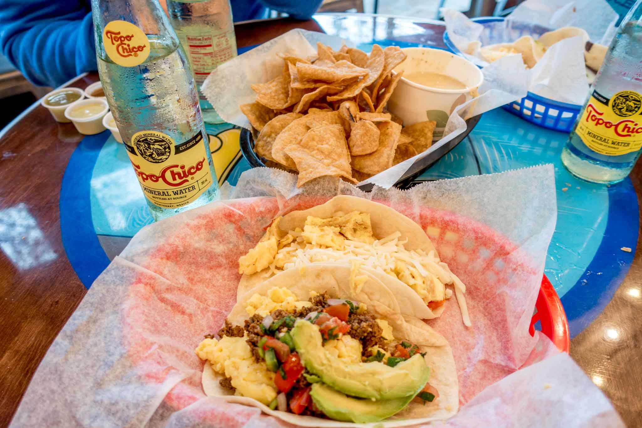 Breakfast tacos, chips, queso, and Topo Chico on a table at Tacodeli