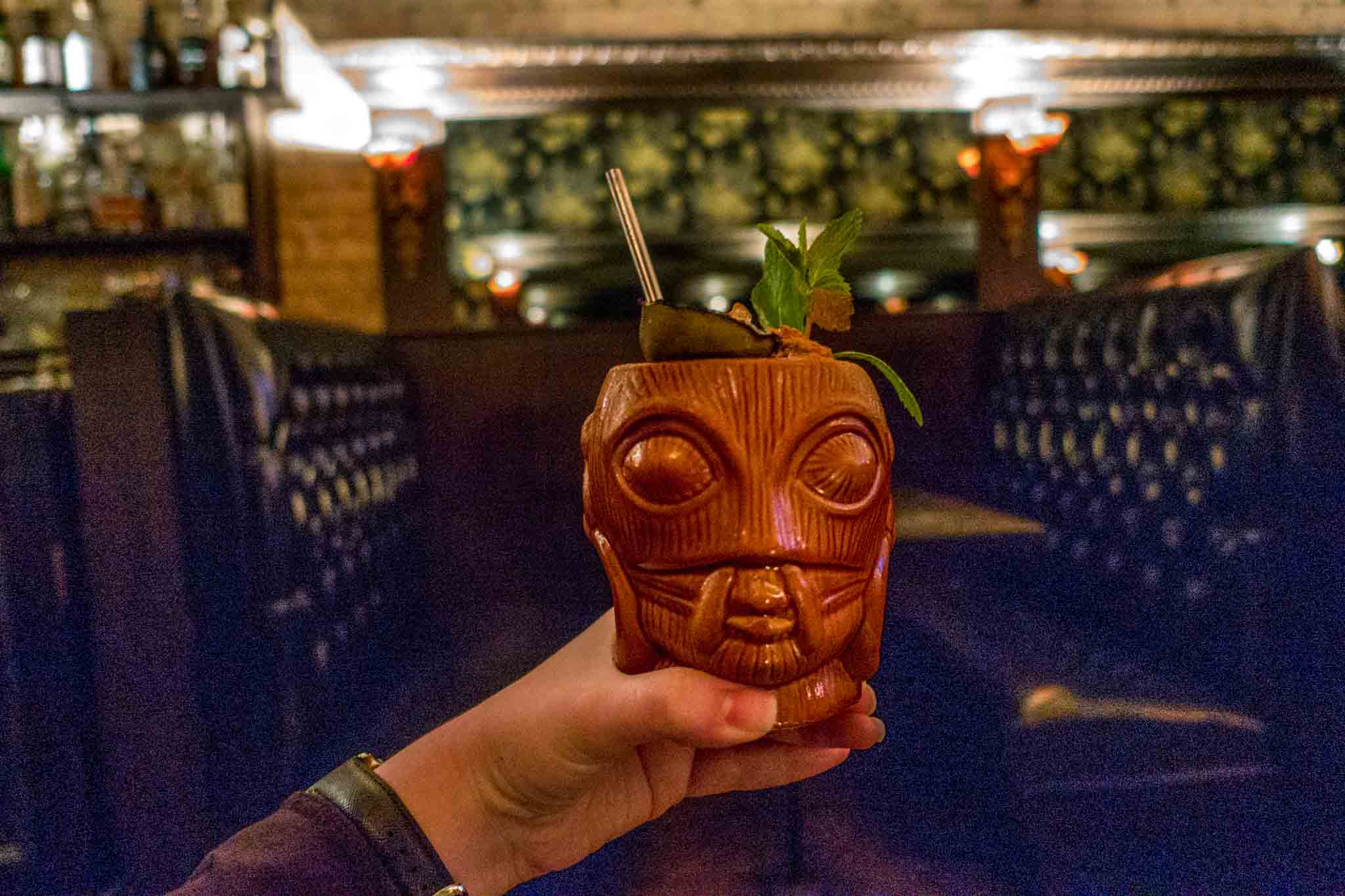 Hand holding a tiki glass in a bar. Trying a tiki drink at a speakeasy like Midnight Cowboy is one of the fun things to do in Austin at night.