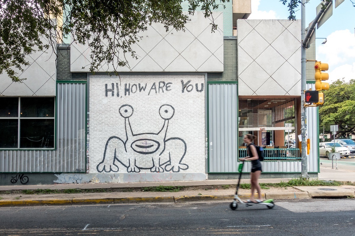 Woman on scooter in front of mural showing cartoon frog