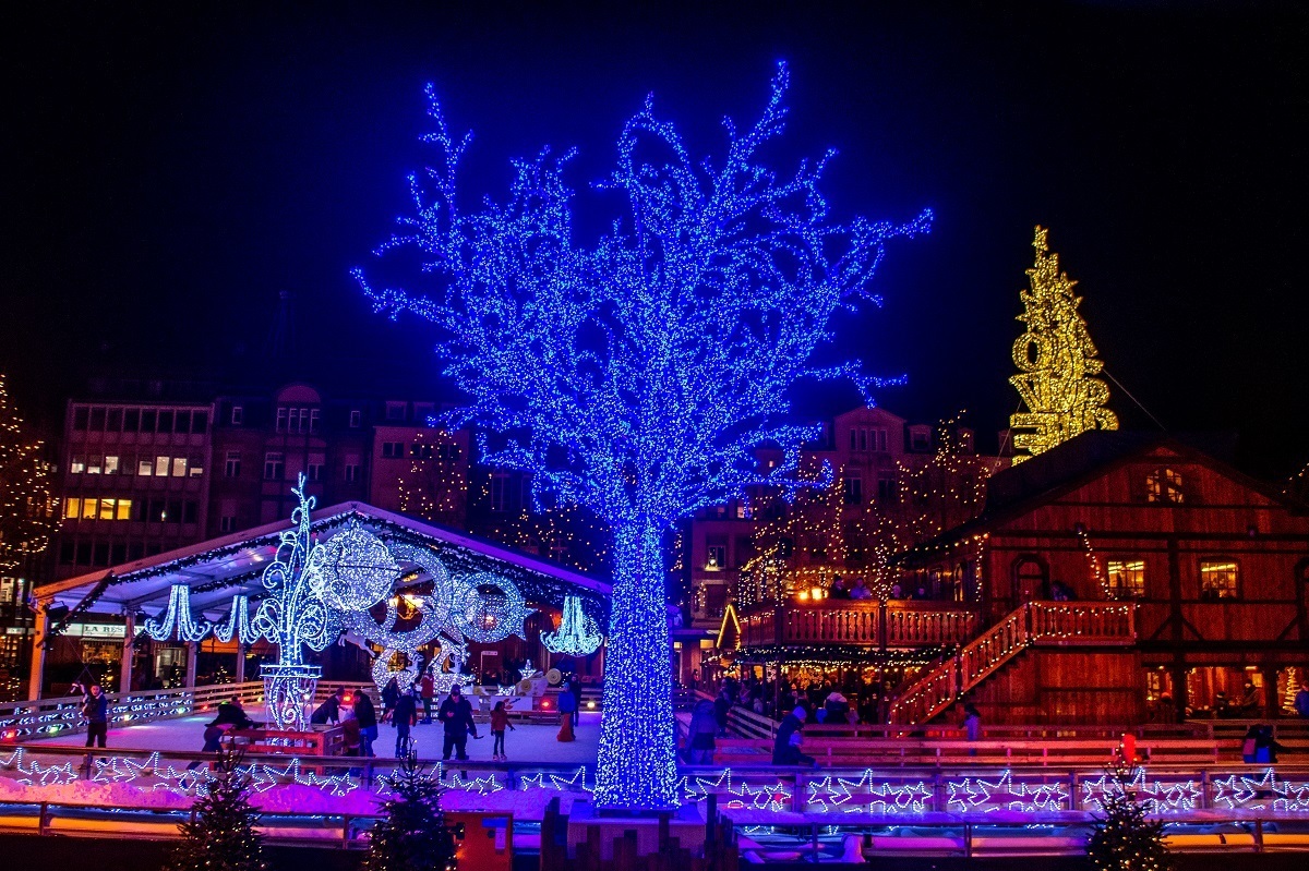 Illuminated ice skating rink, tree, and food stalls at night in Luxembourg City