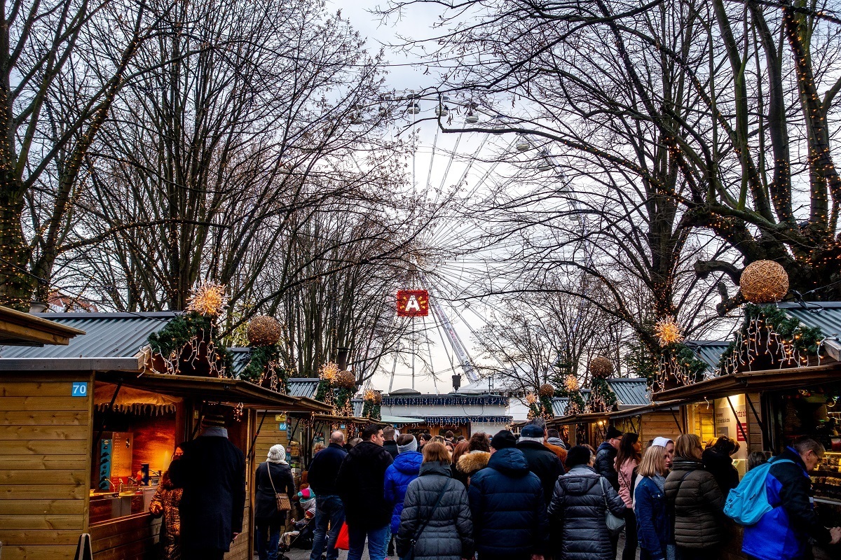 People shopping at Antwerp market stalls with Ferris wheel in the distance
