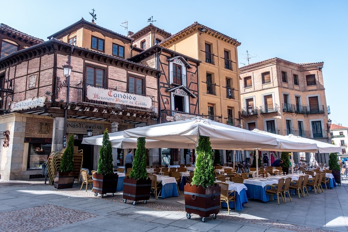 The exterior of Meson de Candido with outdoor seating under large umbrellas. This restaurant features the Segovia specialty of roasted suckling pig.