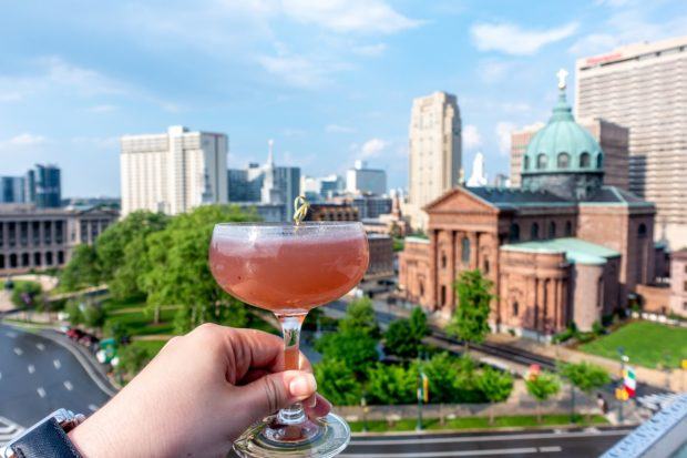 Cocktail glass in front of a skyline view of Philadelphia. Having a drink at one of the rooftop bars is one of the cool things to do in Philly.