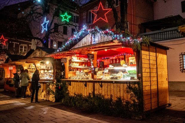Stand selling cheese that is lit up at night with red and green Christmas lights in Place des Meuniers, part of the Strasbourg Noel market