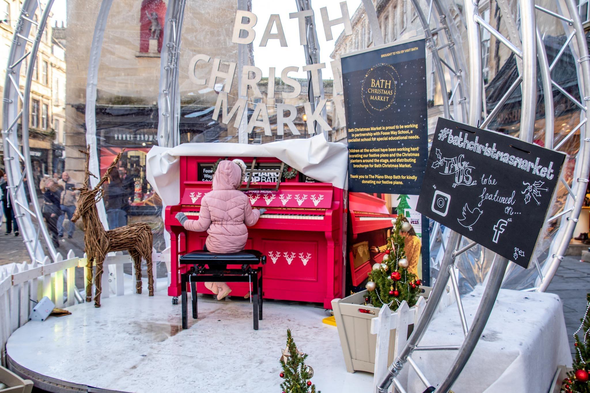 Girl in pink coat playing piano outside at Bath Christmas market