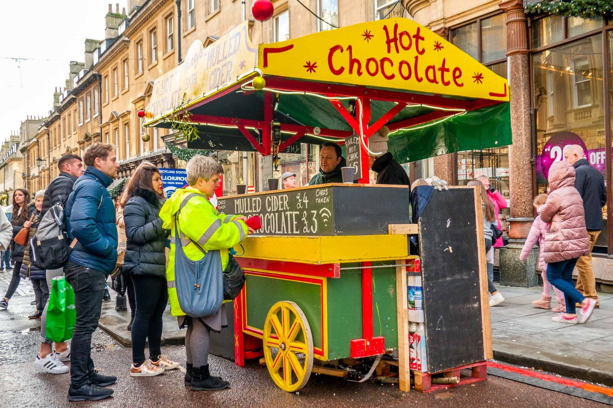 People standing at yellow and green hot chocolate cart in the street in Bath, England