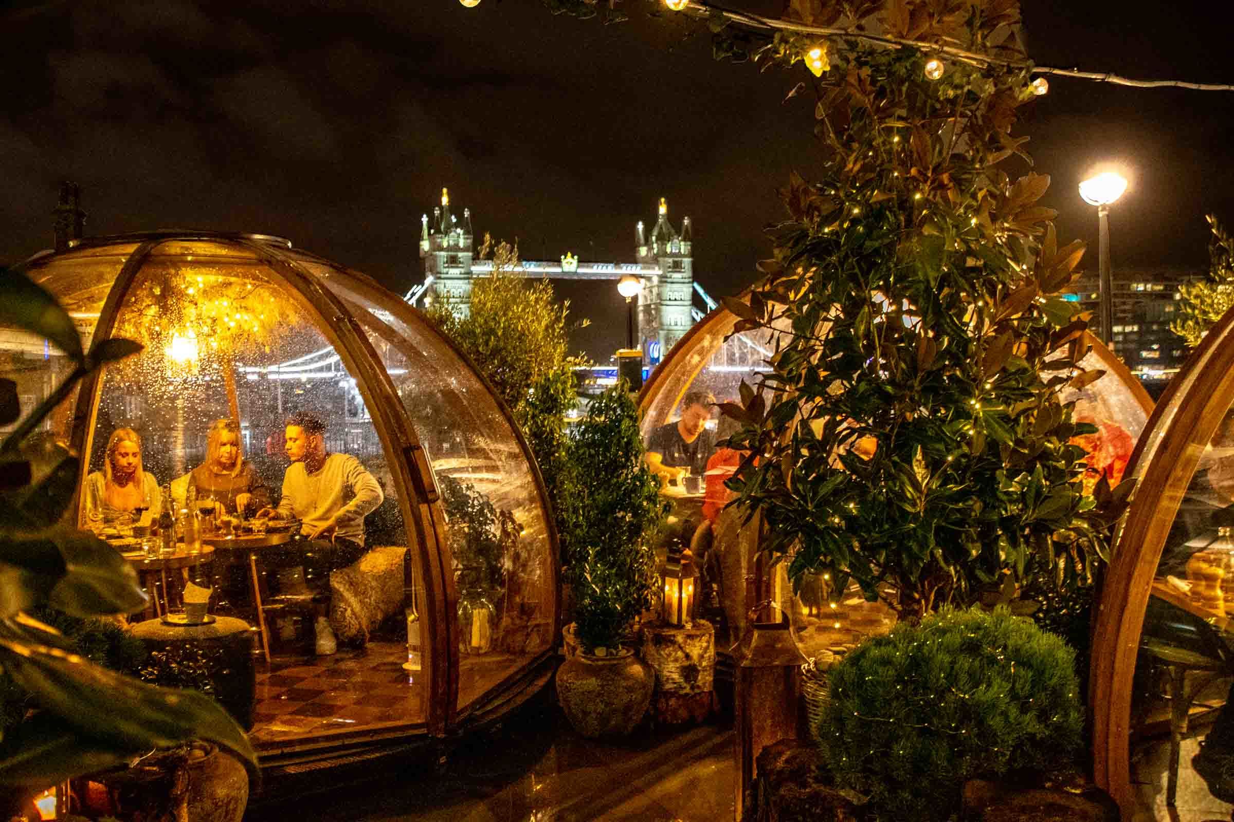People sitting in transparent igloos overlooking the famous Tower Bridge in London