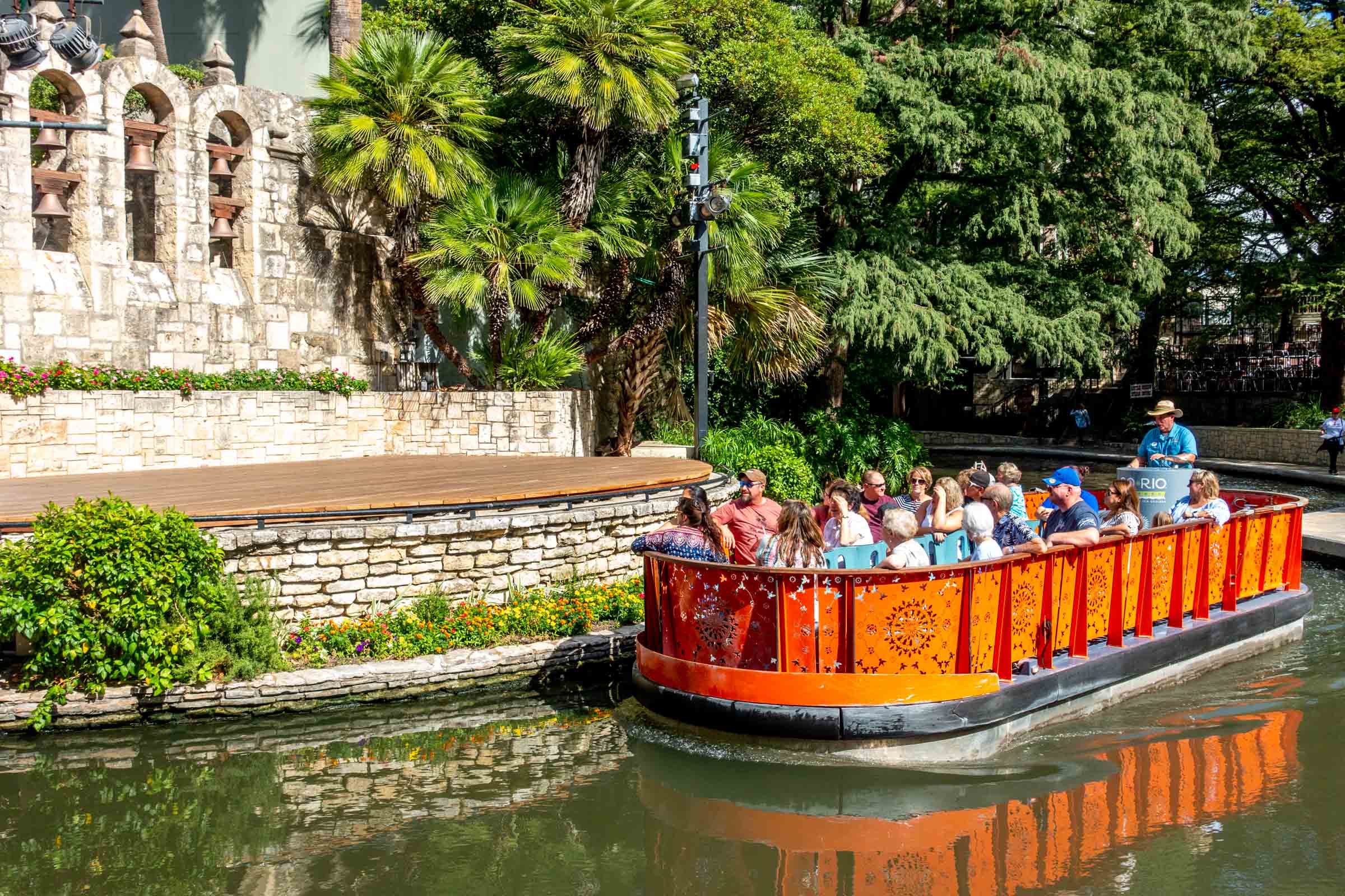 Orange boat filled with people in river along San Antonio RiverWalk