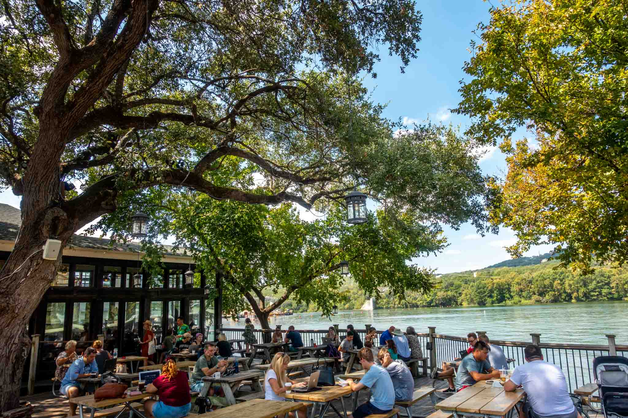 People sitting at picnic tables on a patio by Lake Austin