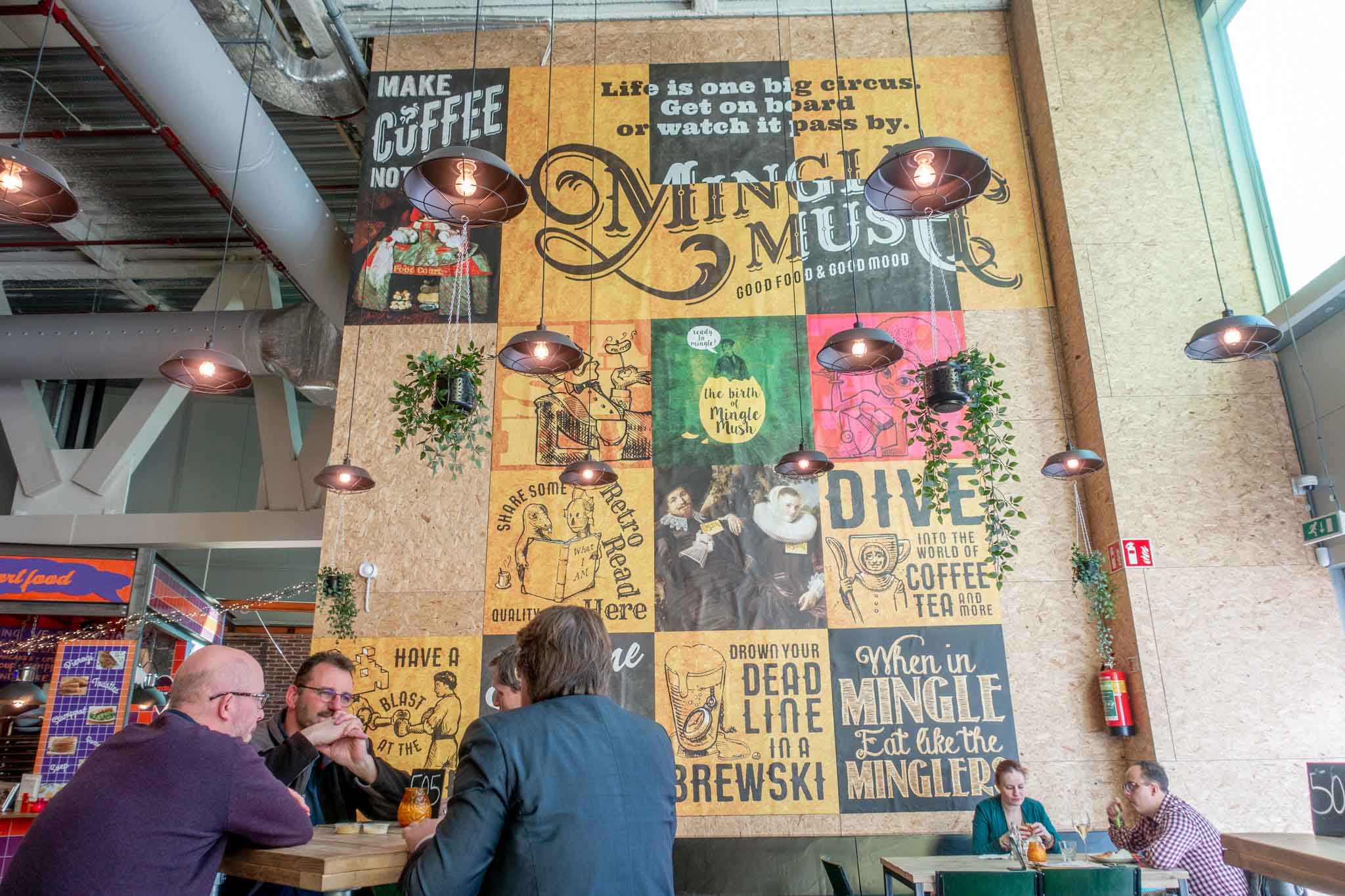 People eating at tables beside a wall decorated with posters