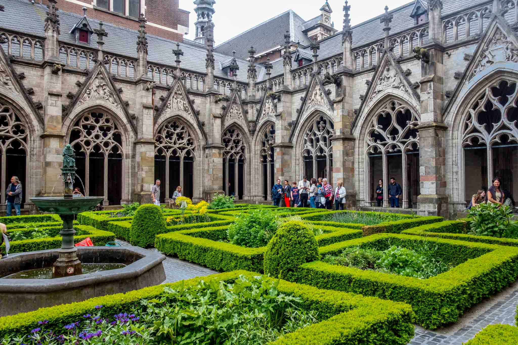 People in a garden surrounded by stone cloister building